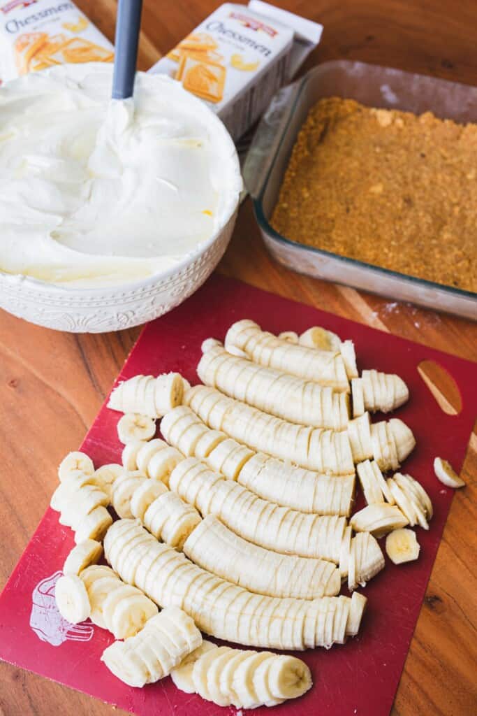 Sliced bananas and cream mixture sit beside dish with pressed graham cracker crust and packages of Chessmen cookies.