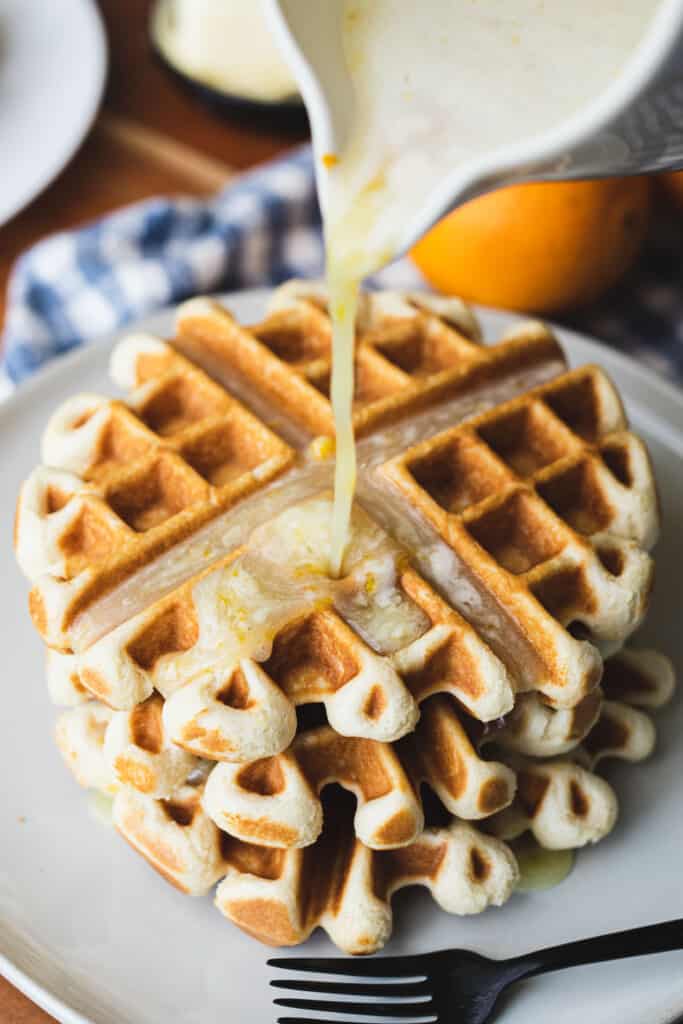 Orange blonde butter syrup pours out over a stack of golden waffles ready for eating.