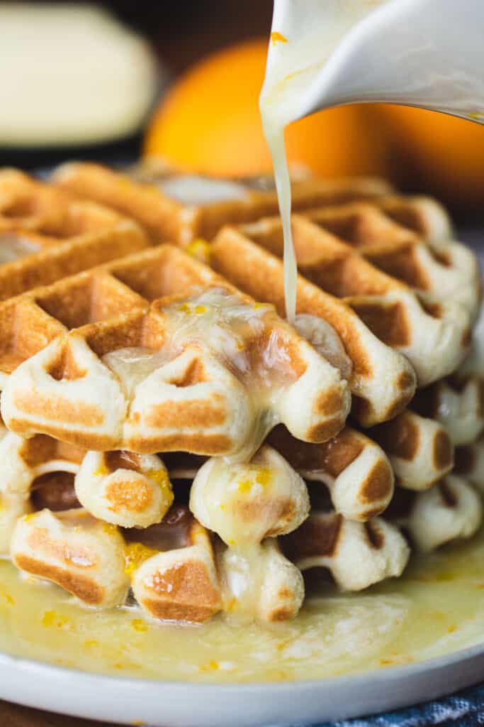 Syrup drizzles out of a ceramic dispenser on to a stack of golden waffles.