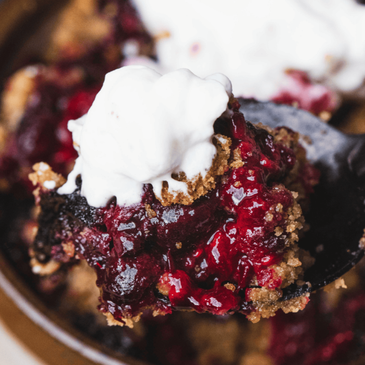 A warm spoonful of Triple Berry Crumble, topped with homemade whipped cream is ready for tasting.