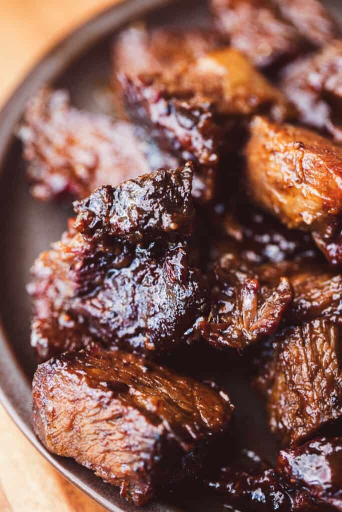 Flavorful and tender burnt ends covered in sweet honey bbq sauce sit on a plate.