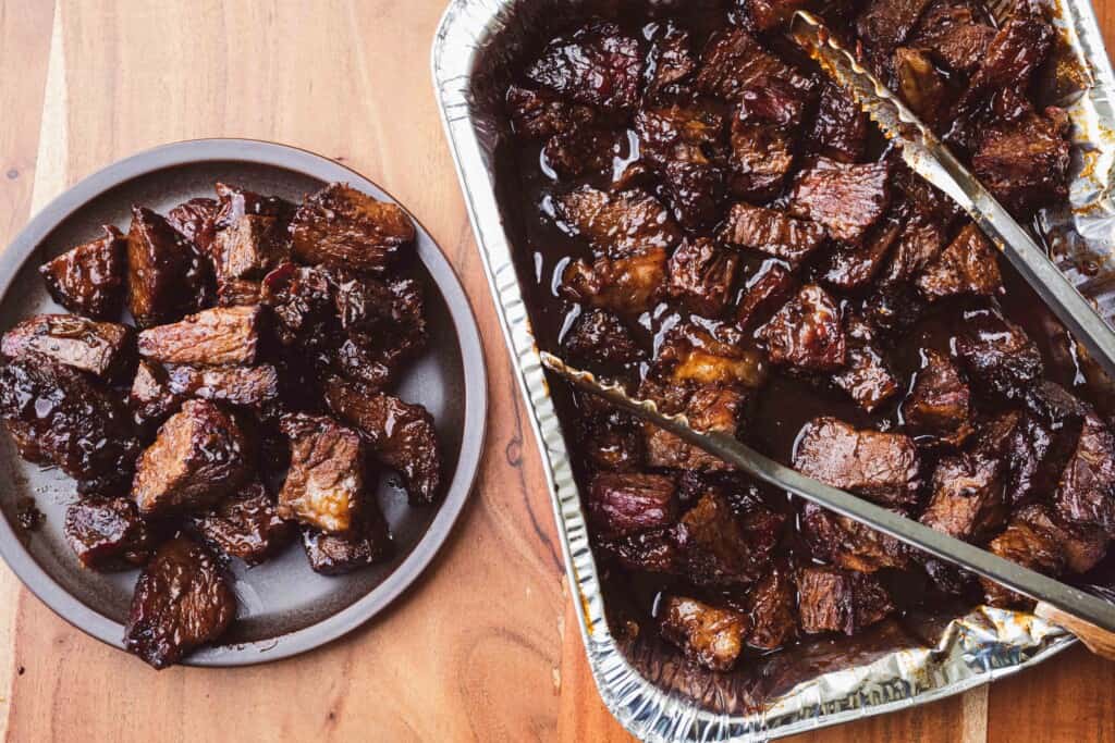Tray of burnt ends sits beside a plate of served meat, ready to enjoy.