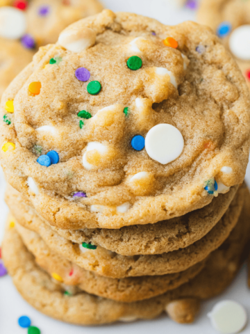 Five cookies sit stacked one on top of the other with sprinkles and chocolate chips scattered around.