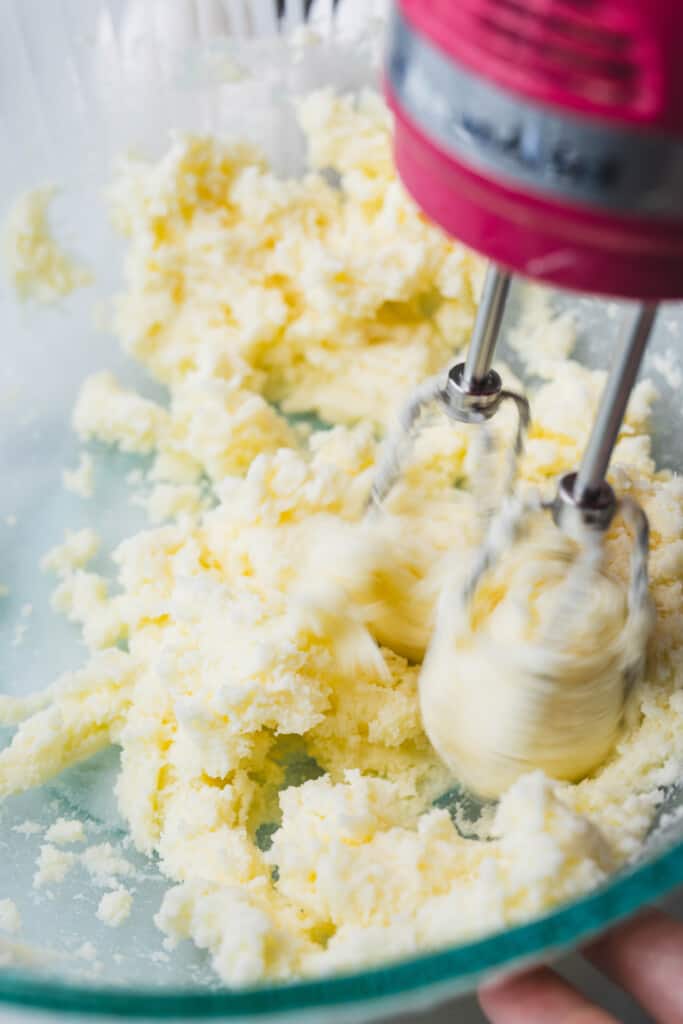A hand mixer creams together butter and sugar in a large glass bowl.