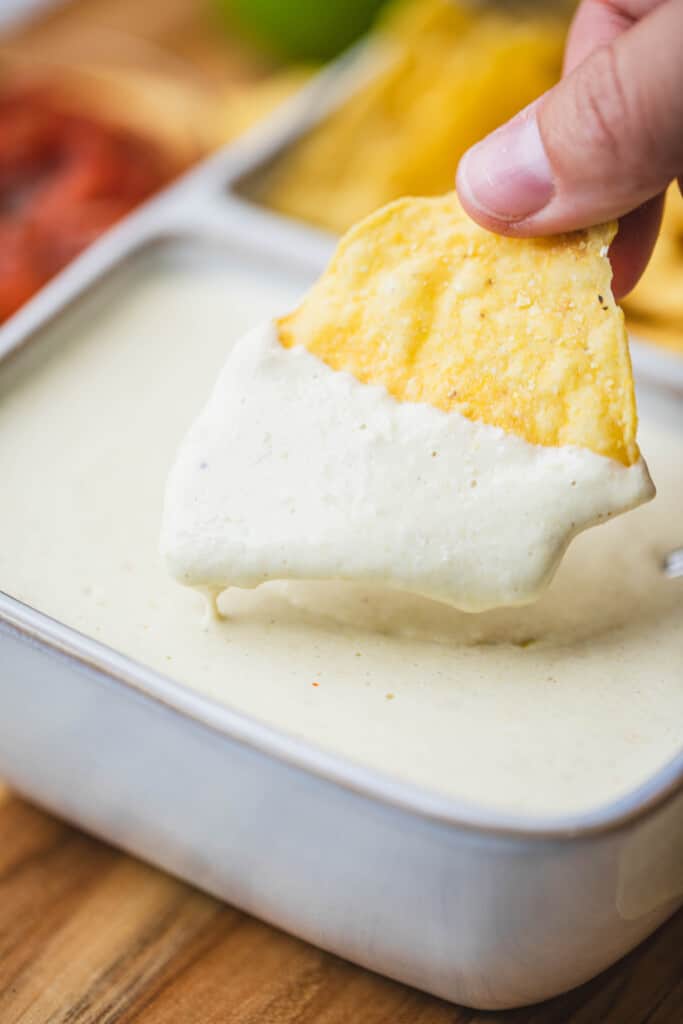 A hand pulls a chip from a serving tray filled with Queso Blanco.