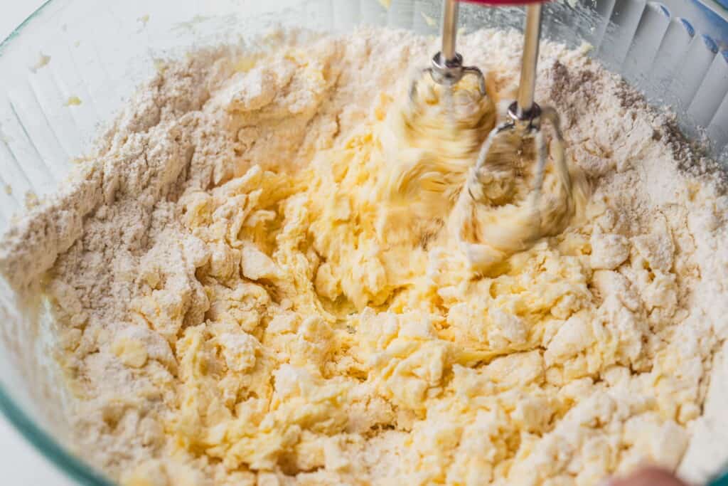 A hand mixer incorporates flour into a bowl of dough.