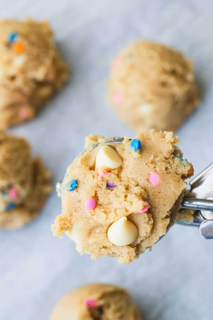 A medium scoop is full of prepared cookie dough and is held over a cookie sheet covered with parchment paper.