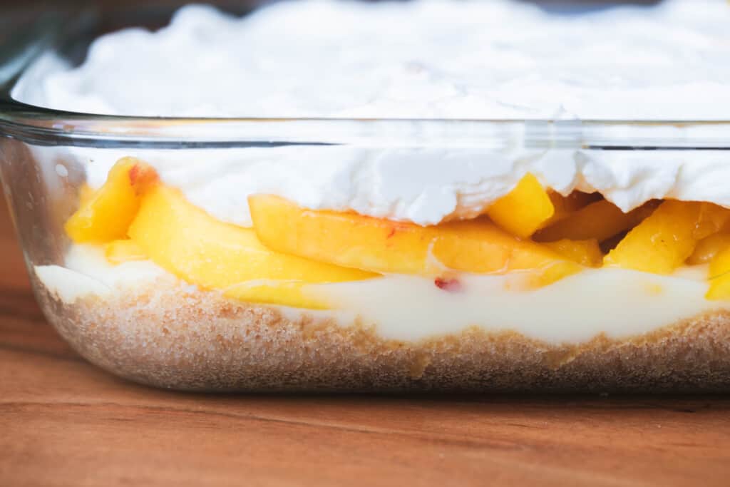 Layered Peaches and Cream dessert sits in glass dish for chilling.