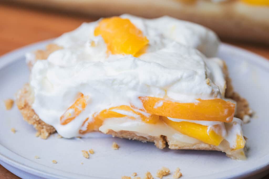 Serving of Peaches and Cream Layered Dessert sits on a white plate ready for eating.