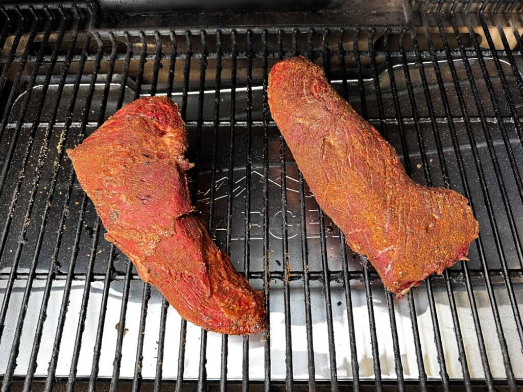 Two seasoned tri-tip steaks sit on Traeger grill to be cooked on low heat.