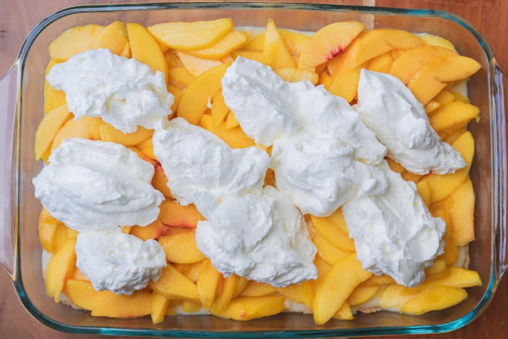 Dollops of whipped topping sit on top of sliced peaches to make the final layer.