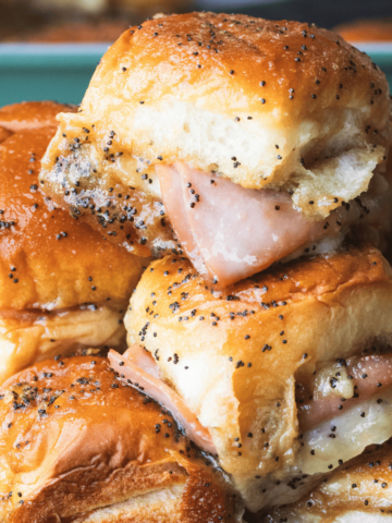 Ham and cheese sliders are stacked on a plate, toasty, melty and ready to enjoy.