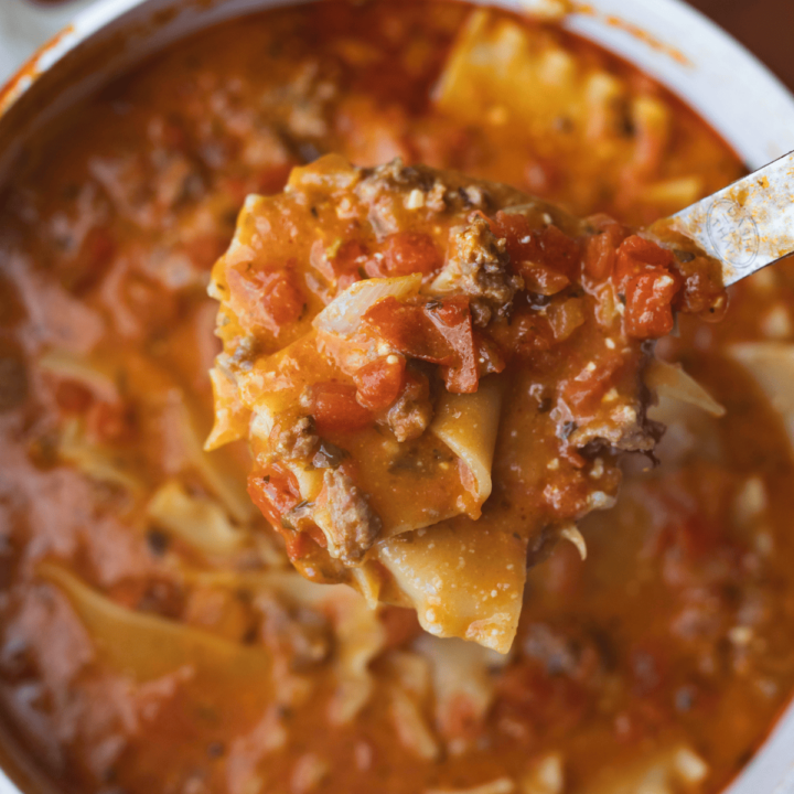 Ladle held over a large pot is full of sausage, tomatoes, noodles of One Pot Lasagna Soup.