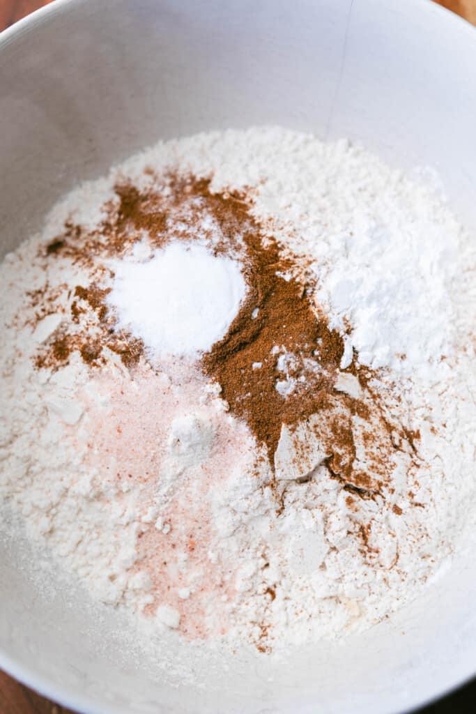 Dry ingredients like flour, cinnamon, salt, cream of tartar, baking soda sit in a bowl.