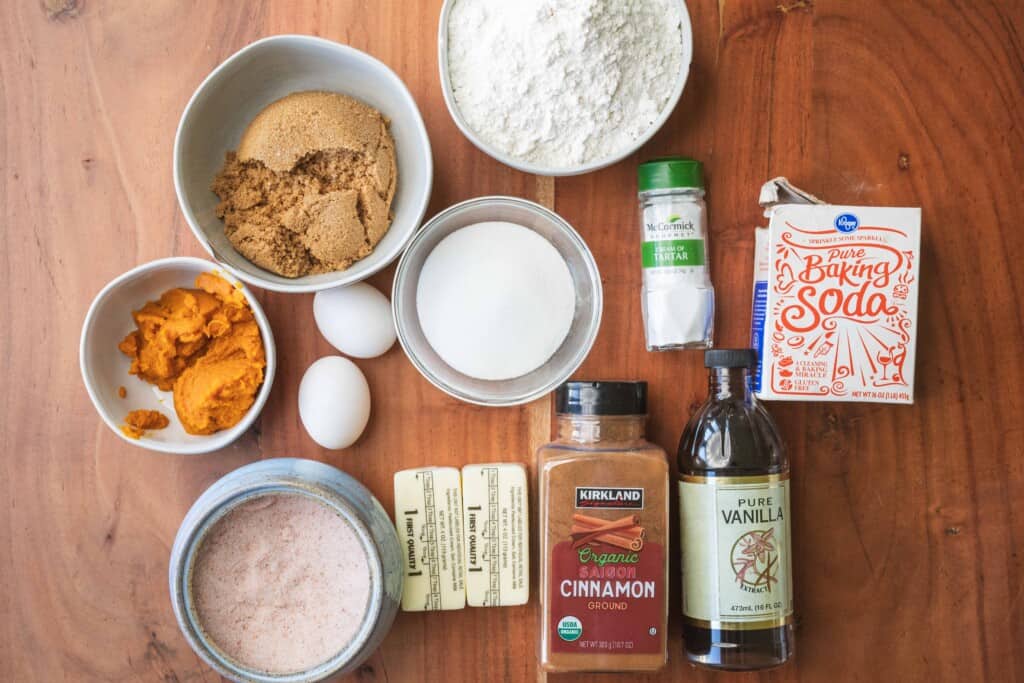 Ingredients for pumpkin snickerdoodle cookies sit on a wooden counter.