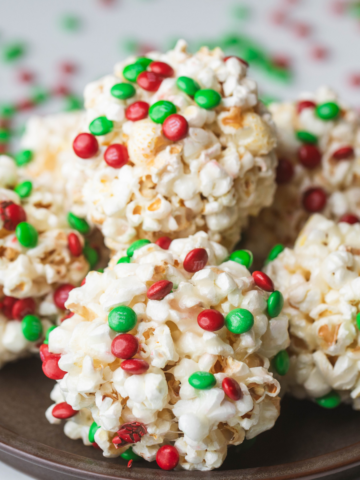 Popcorn balls sprinkled with red and green candies are stacked on a dark plate.