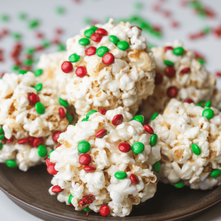 Popcorn balls sprinkled with red and green candies are stacked on a dark plate.
