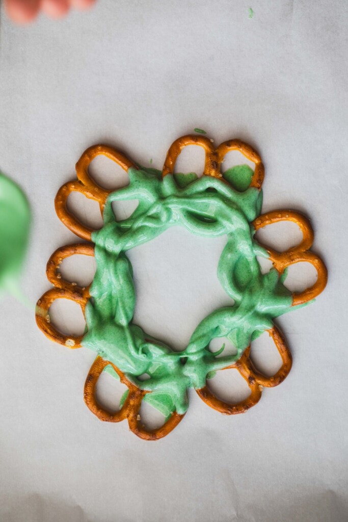 Pretzels laid out in a circle are drizzled with the dyed white chocolate around the center ring creating the base layer.