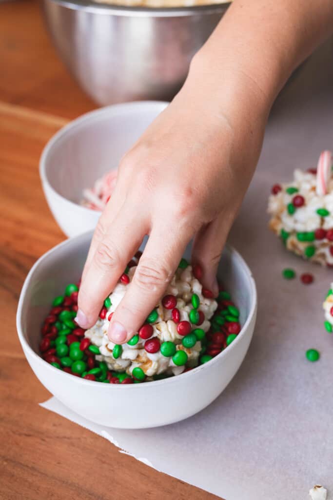 A hand holds a formed treat and dips it into a bowl of mini m&m's.