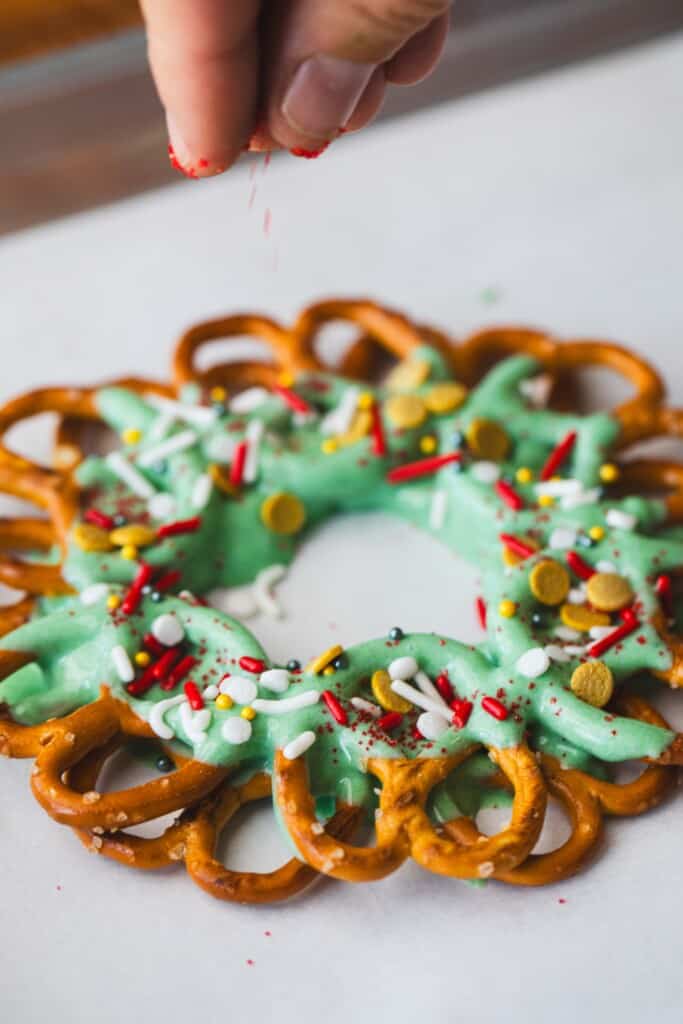A hand scatters red sprinkles over the candy wreath.