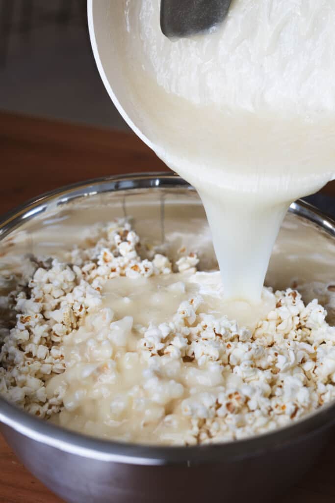 A cream syrup mixture is poured over a metal bowl filled with fresh popped corn.