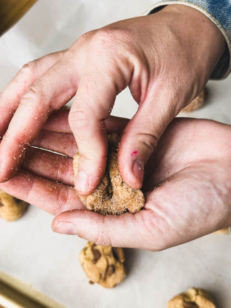 Hand pinches cookie dough together after being rolled in cinnamon sugar.