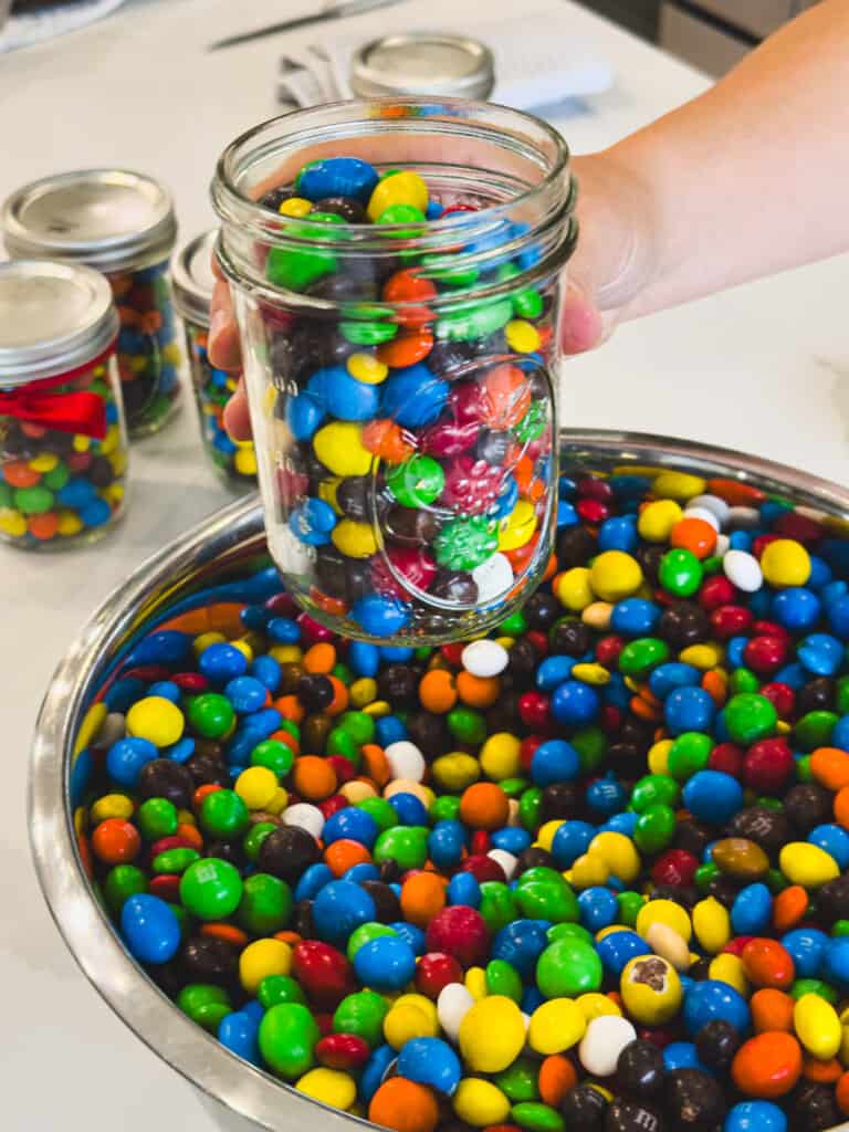 A hand holds a glass mason jar full of colorful chocolate candies.