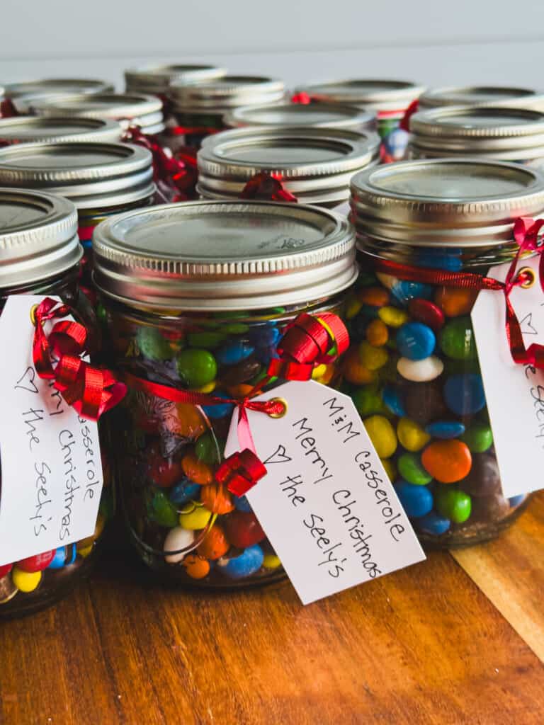 Glass mason jars filled with chocolate candies sit on a tabletop with Christmas notes attached.