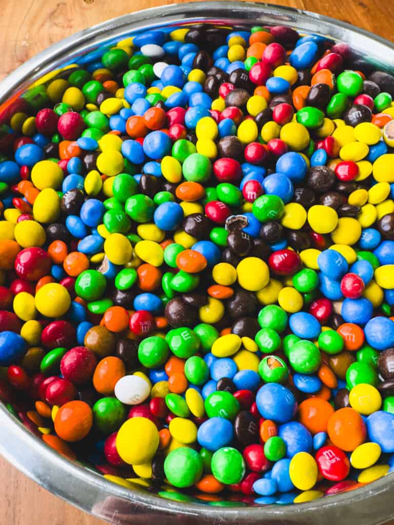 A large metal bowl is filled with colorful chocolate candies.