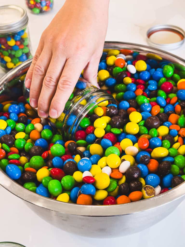 A hand holds a glass mason jar scooping it up and filling it with colorful chocolate candies.