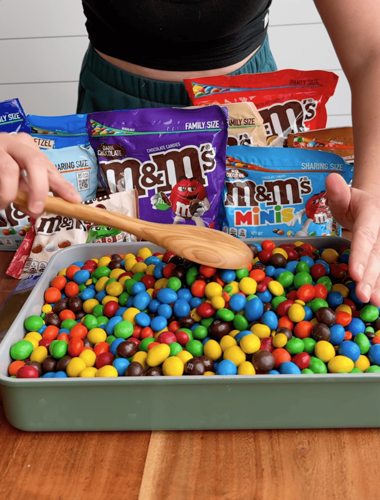 A wooden spoon stirs up ten different flavors of chocolate candies in a baking dish.