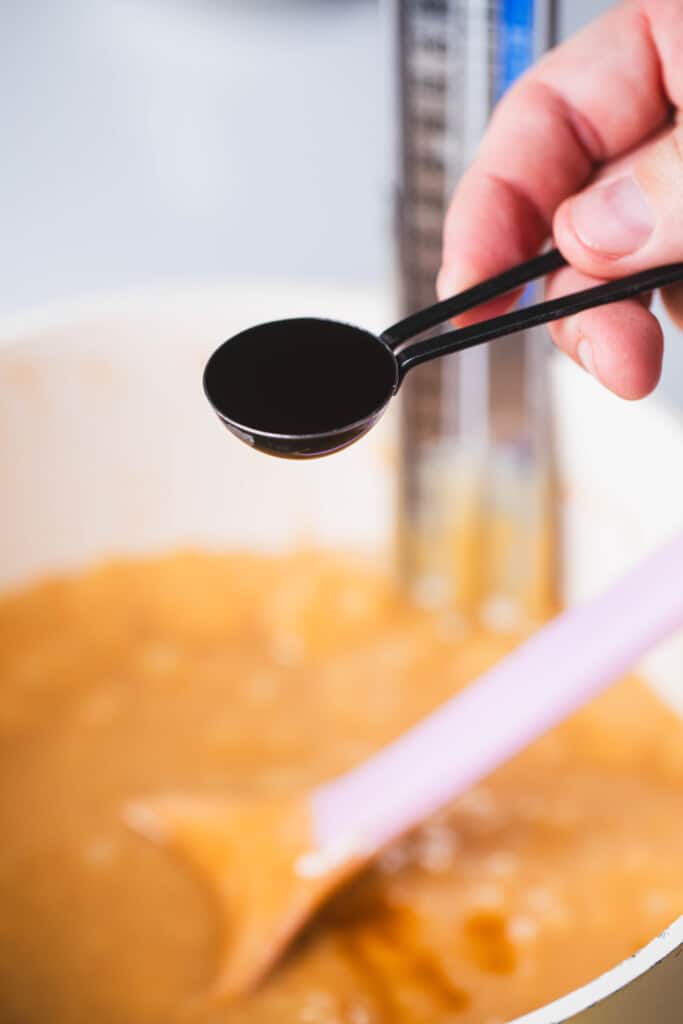 Measuring spoon of vanilla is held over pot with mixture.