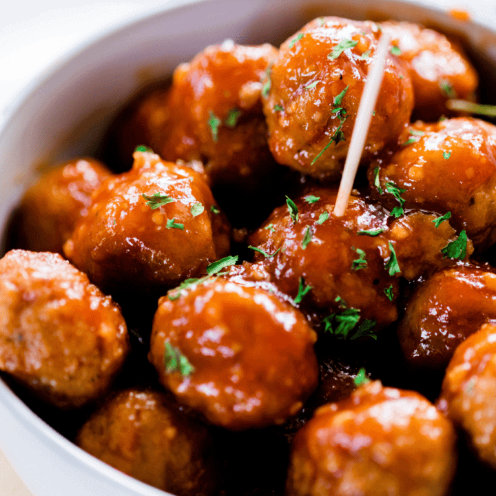 Honey garlic meatballs sit in a white bowl with a toothpick inserted for snacking.