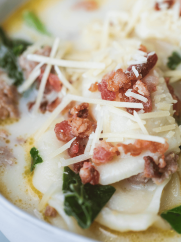 White bowl filled with pierogi soup is topped with fresh parmesan and crumbled bacon.