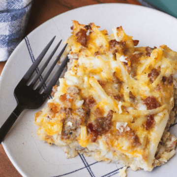 A serving of Amish Breakfast Casserole sits on a plate with a fork ready for enjoying.