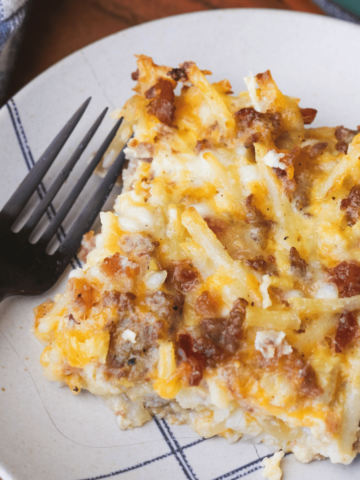 A serving of Amish Breakfast Casserole sits on a plate with a fork ready for enjoying.