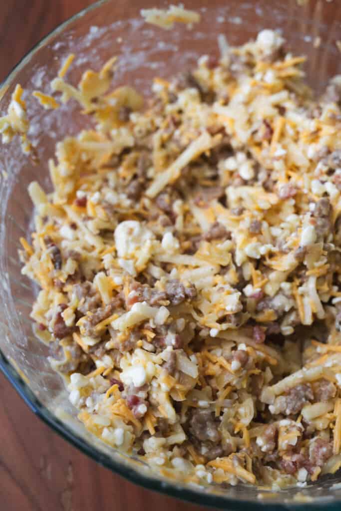 Hash browns, eggs, sausage, cheese and other ingredients are mixed in a large glass bowl.