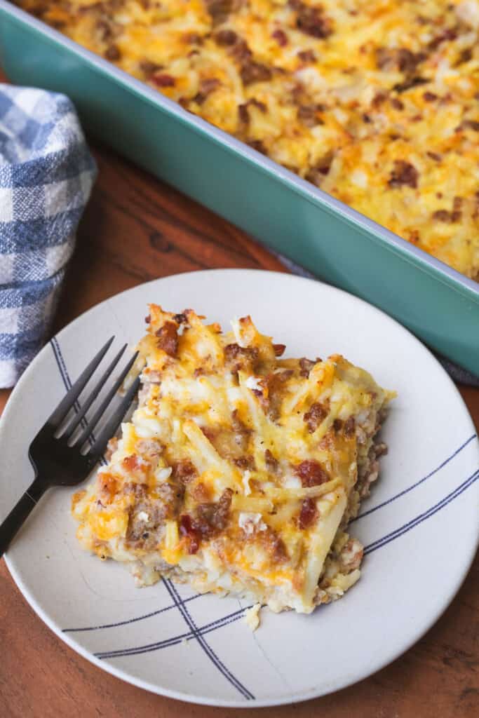 A serving of Amish Breakfast Casserole sits on a plate with a fork ready for enjoying.