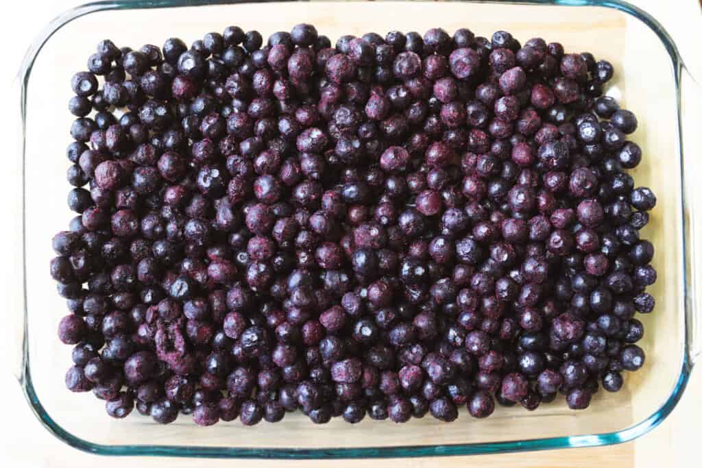 Berries sit in the bottom of a glass baking dish.