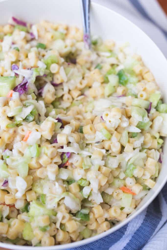 Creamy Coleslaw Pasta Salad sits in a white serving bowl with a metal spoon.