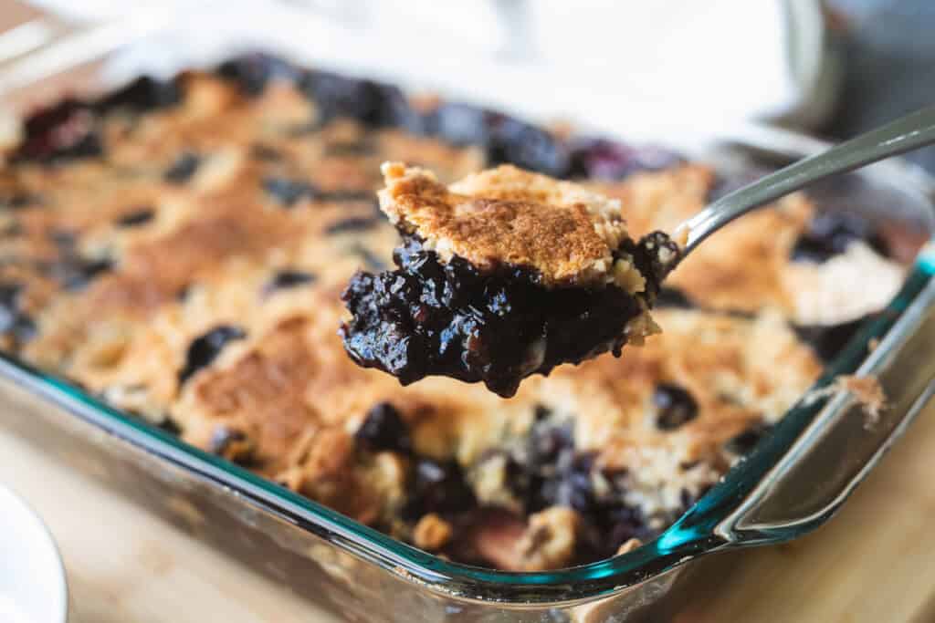 Spoonful of berry cobbler is scooped from a warm baking dish ready to serve.