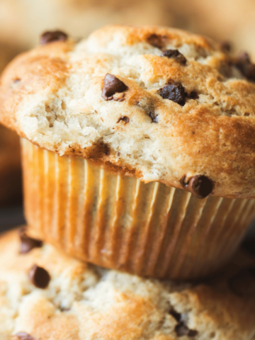 A golden brown Banana Chocolate Chip Muffin sits on top of another muffin.