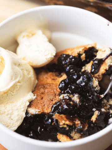 Warm bowl of blueberry cobbler is served a la mode with a spoon.