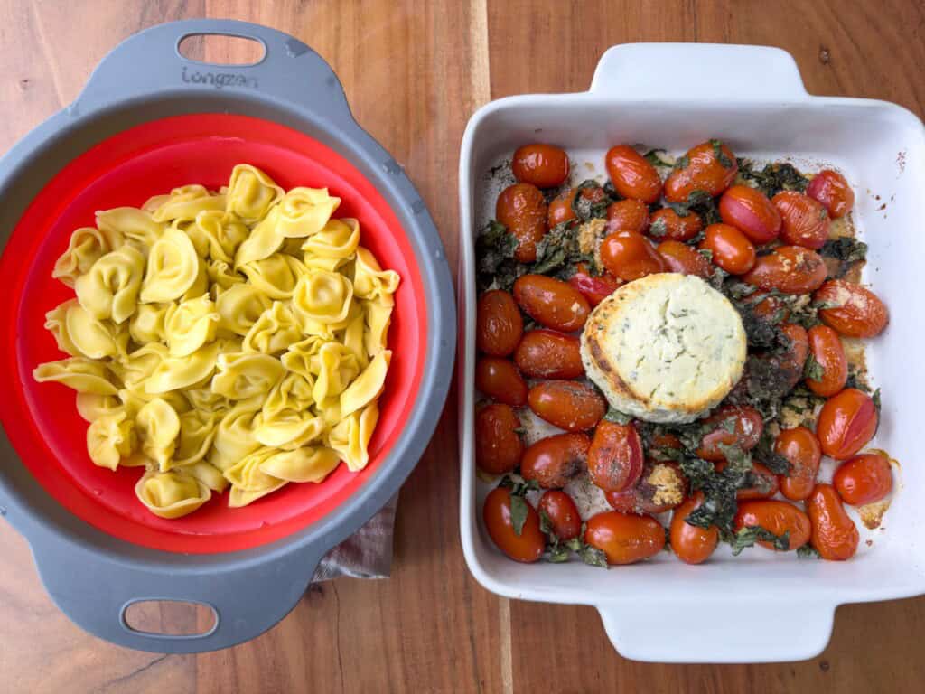 Cooked tortellini sits in a colander beside a baking dish of roasted tomatoes, basil and cheese.