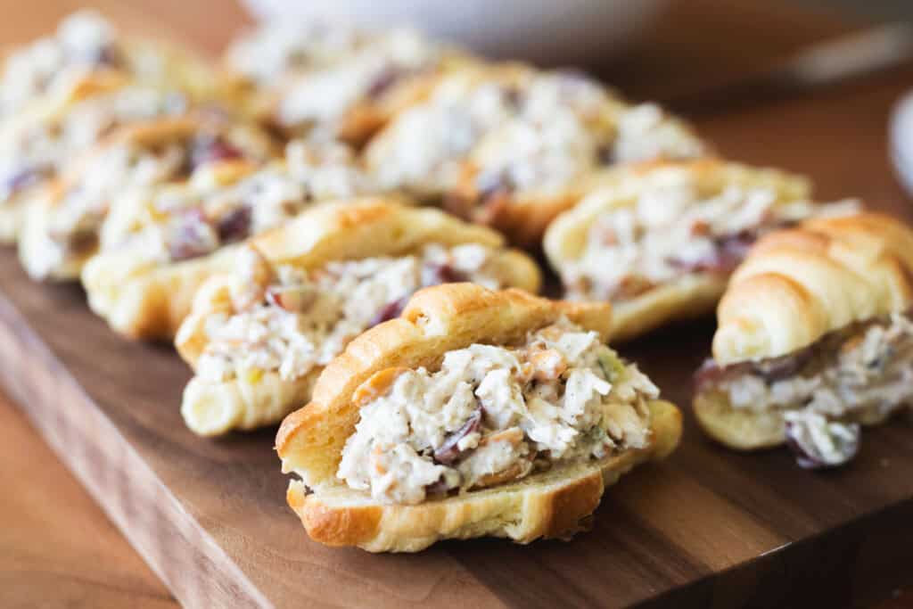 Two rows of chicken salad sandwiches sit on a wooden board.