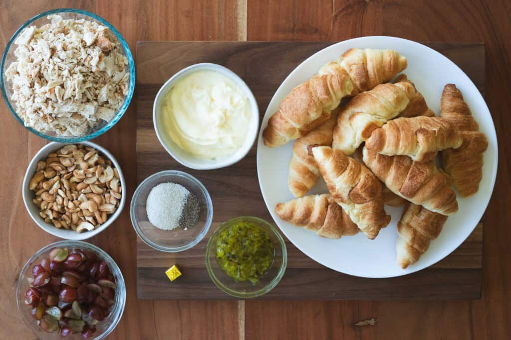 Ingredients for chicken salad sandwiches sit out on a wooden countertop for preparing.