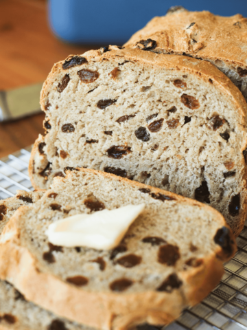 Slices of cinnamon raisin bread sit on a cooling rack with a slab of butter.