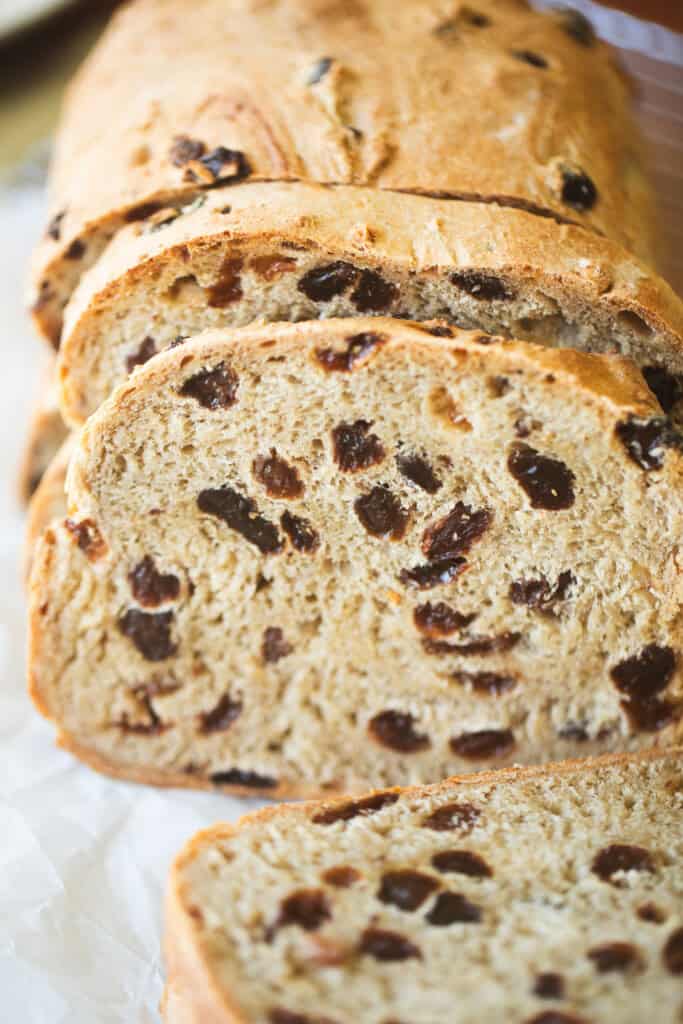 A loaf of cinnamon raisin bread sits on a towel with a few slices.