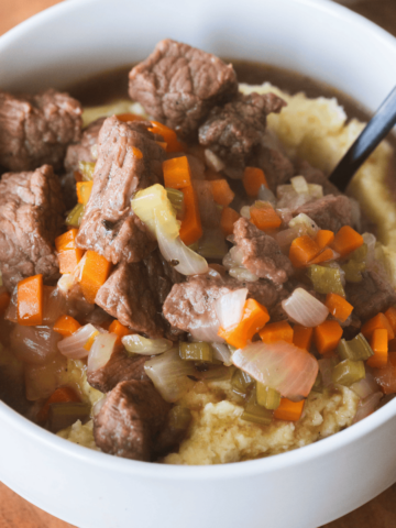 Chunks of tender beef and veggies are served over fluffy mashed potatoes and savory broth.