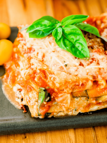 Slice of zucchini and pesto lasagna sits on a plate ready to eat. It is garnished with fresh basil leaves.